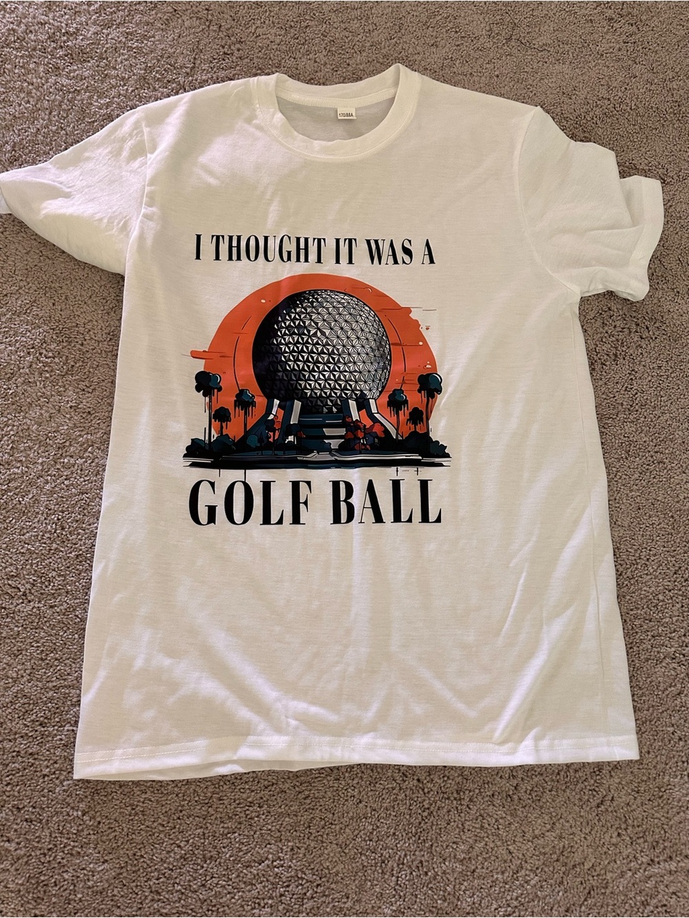Graphic Tee — 'I Thought It Was A Golf Ball' in White with Orange & Black Print